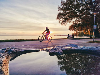 Rear view of man riding bicycle on beach against sky during sunset