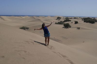 Carefree woman with arms outstretched standing on sand at desert during sunny day