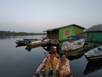 Rear view of men standing on boat moored in lake against sky