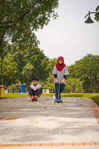 Children riding skateboard and scooter in the park.