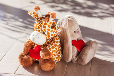 Children's soft plush toy giraffe and bunny sit on wooden background, hard light and shadow