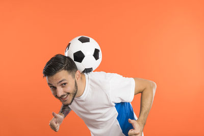 Portrait of boy playing soccer ball against yellow background