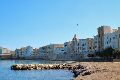 Buildings by sea against clear blue sky