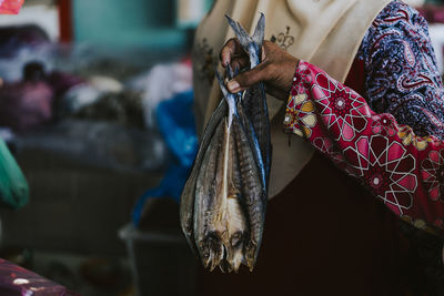 Cropped hand of woman holding fishes in market