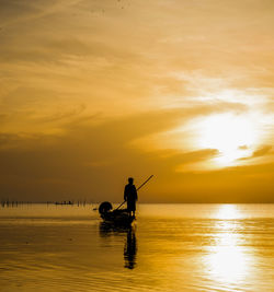 Silhouette man fishing in sea against sky during sunset