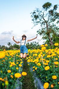 Young woman jumping amidst flowering plants on field