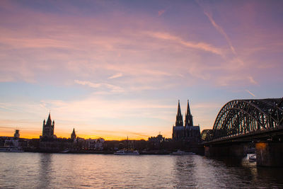 Arch bridge over river by buildings against sky during sunset