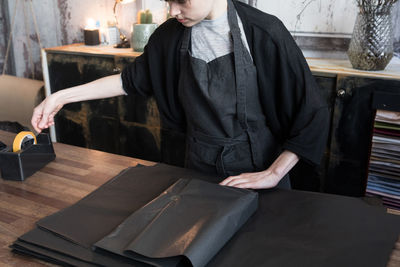 Midsection of young female owner packing with wrapping paper on counter at store