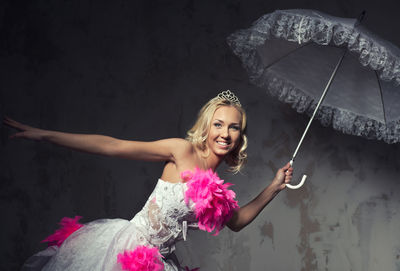 Portrait of beautiful young woman in pink and white wedding dress posing with umbrella against wall