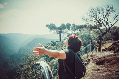 Side view of woman with arms outstretched standing on mountain against sky