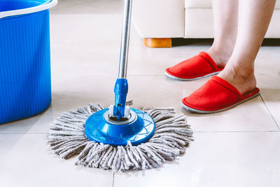 Low section of woman cleaning tiled floor with mop at home