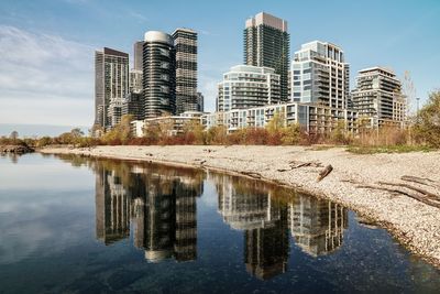 Reflection of buildings in lake against sky in city