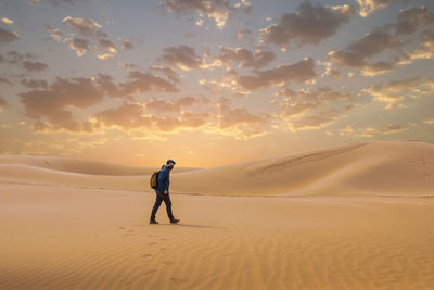 Man on sand dune in desert against sky during sunset