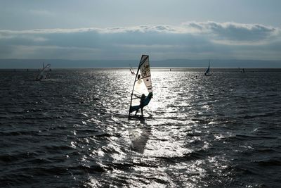 Woman windsurfing in sea against sky on sunny day