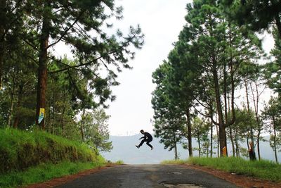 Man jumping on road amidst trees against sky