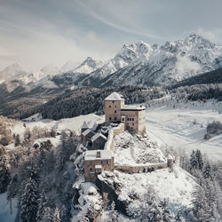 View of building on snowcapped mountains against sky during winter