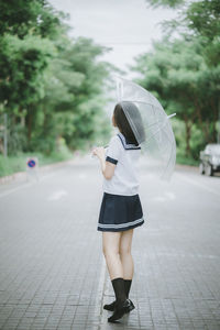 Young woman with umbrella standing on road