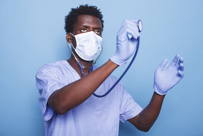 Midsection of doctor holding dentures against blue background