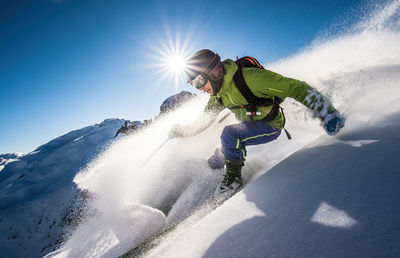 Man skiing on snowcapped mountain against sky during winter