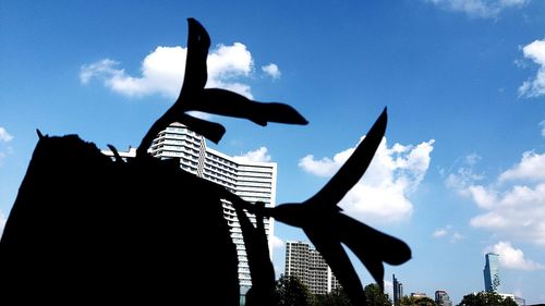 Low angle view of silhouette statue against buildings in city against sky