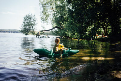 Side view of boy sitting on crocodile shape pool raft at lakeshore