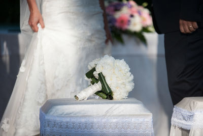 Midsection of bride and groom with bouquet on table
