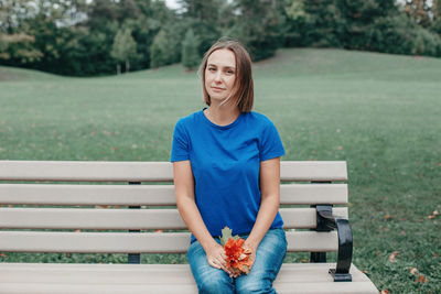 Portrait of young woman sitting on bench in park