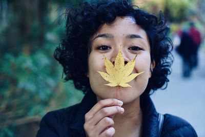 Portrait of woman holding maple leaf against mouth