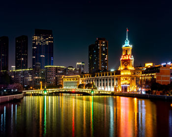 Illuminated buildings by river against sky at night