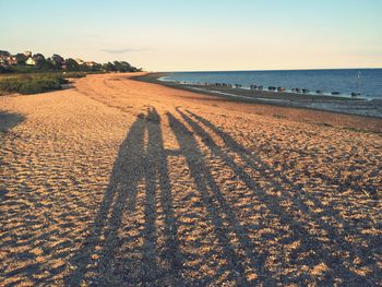 Shadow on people at beach against sky during sunset