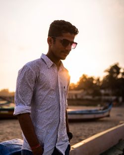 Young man wearing sunglasses while standing against sky during sunset