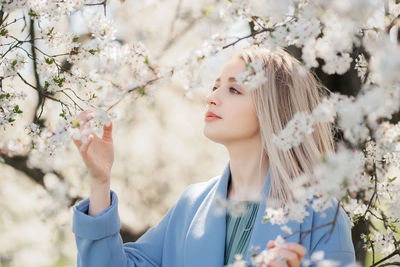Portrait of young beautiful blonde woman posing in blooming white apple flowers on branches