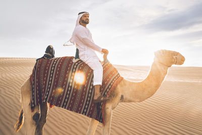 Rear view of woman riding horse on sand against sky