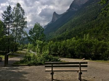 Bench against trees and mountains against sky