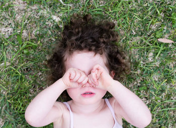 High angle view of girl rubbing eyes while lying on grassy field