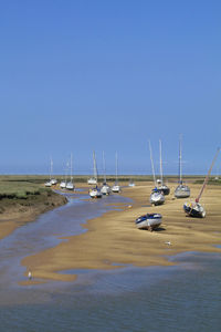 Sailboats moored on sea against clear blue sky