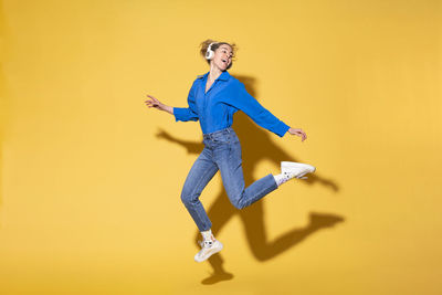 Carefree young woman listening to music against yellow background