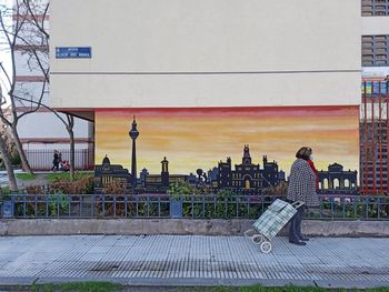 Side view of people on bench in city against sky