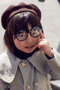 Korean girl in a gray coat and cap and round glasses stands the street in spring.