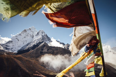 Colorful prayer flags hanging by mountain against blue sky during sunny day