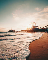 Ferris wheel at beach against sky during sunset