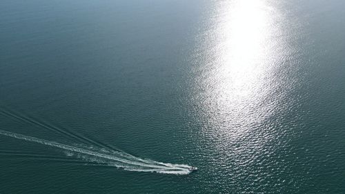 High angle drone view of sea with a moving boat against the reflection of the sun in calm waters