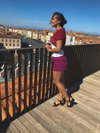 Girl in full growth, standing on the roof, holding on to the railing, looking at the cityscape