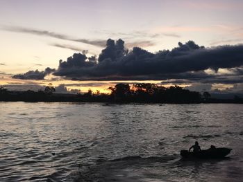 Silhouette people on sea against sky during sunset