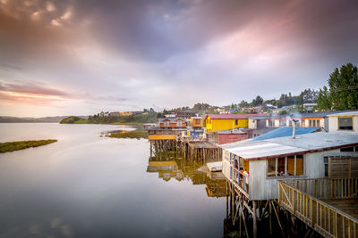 Houses by lake against sky during sunset