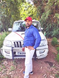 Portrait of young man standing on car against trees