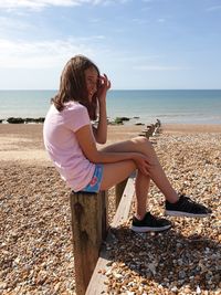 Girl sitting on beach against sea against sky