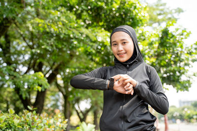 Portrait of smiling young woman standing against trees