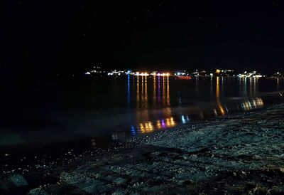 Illuminated city by river against sky at night