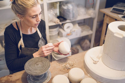 High angle view of woman with ceramics sitting at table in workshop